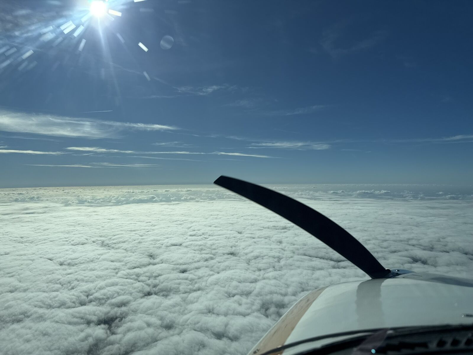 View above the clouds from the cockpit with sunlight streaming in.