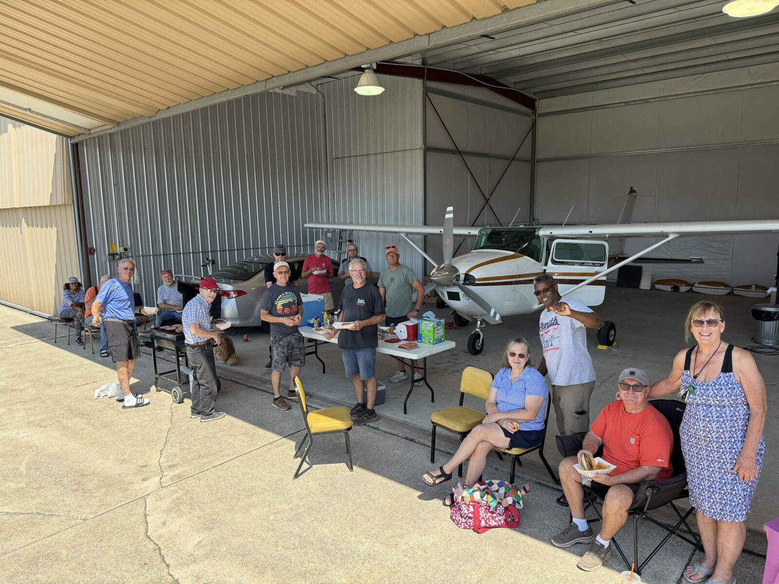 Club members gather for a cookout in a hangar next to a Cessna.